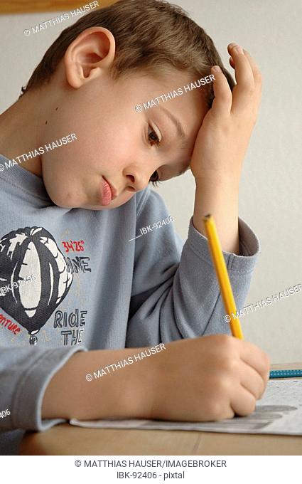 Boy in a blue shirt is sitting at a table and works with paper and pencil
