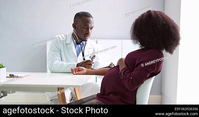 Male Doctor Measuring Blood Pressure Of Pregnant Woman In Clinic