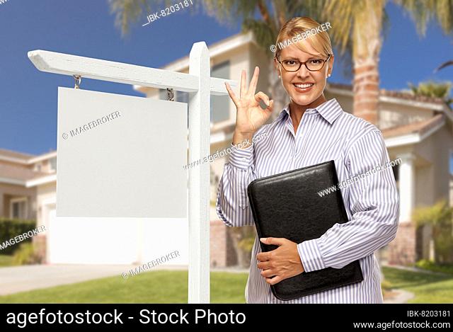 Attractive female real estate agent in front of blank real estate sign and house