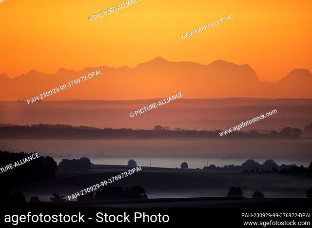 24 September 2023, Baden-Württemberg, Uttenweiler: The rising sun over Upper Swabia colors the sky in orange tones. In the background, the Alps