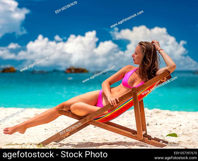 Woman wearing pink bikini in lounger on tropical beach at Thailand