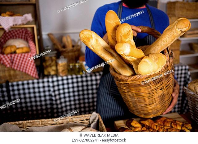 Mid section of staff holding wicker basket of french breads at counter