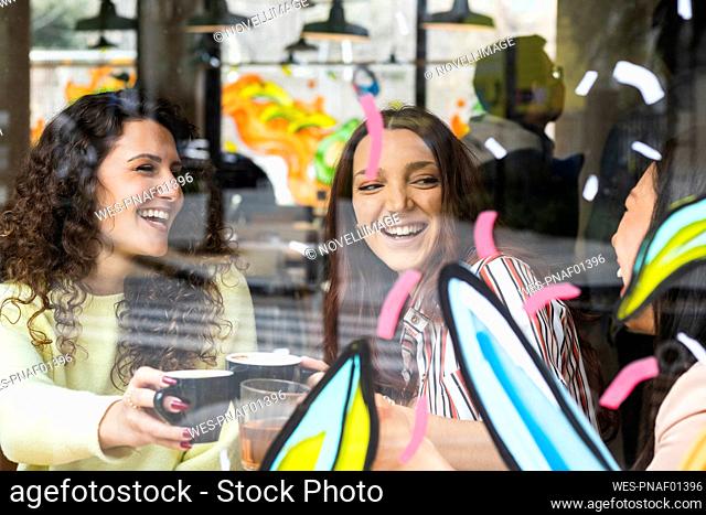 Young female friends smiling while toasting coffee cup at cafe