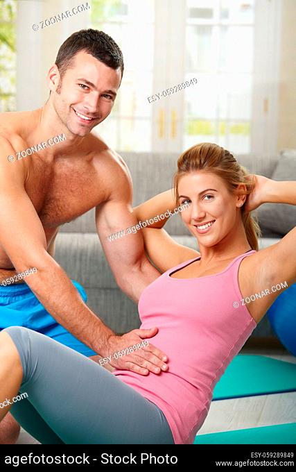 Young woman doing abdominal exercise lying on fitness mat at home in living room
