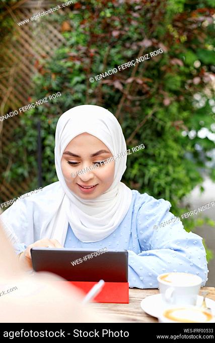 Smiling woman wearing hijab using digital tablet at sidewalk