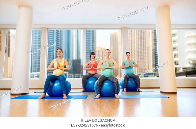 pregnancy, sport, fitness, people and healthy lifestyle concept - group of happy pregnant women exercising on ball in gym over city window view background