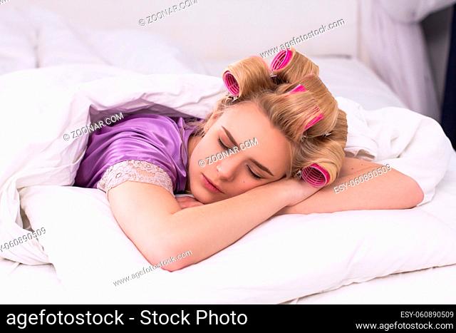 Pretty blond girl laying in bed asleep. Charming young lady wearing purple tee laying on pillow with arms crossed early morning