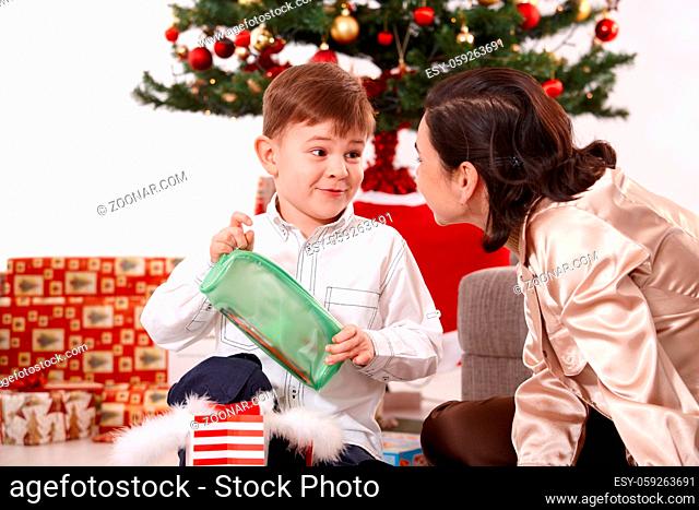 Happy little boy smiling at mum at christmas, holding present