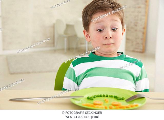 Germany, Munich , Boy eating peas and carrots showing anthropomorphic face