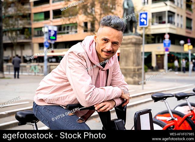 Stylish mid adult man sitting on bicycle against building in city