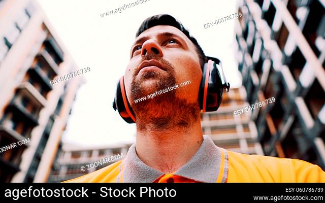 Builder covers his ears, ear muff to protect workers ears. Construction worker wearing protective ear defenders. Concept of construction