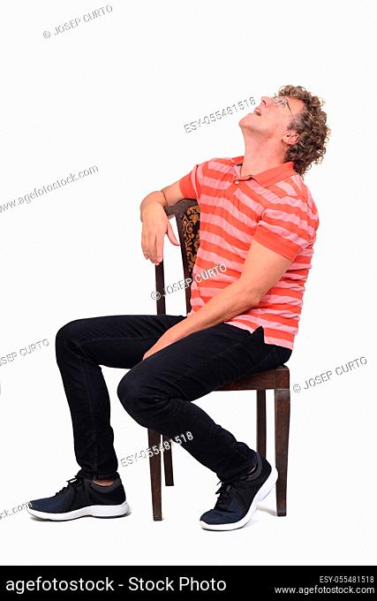 full portrait of a curly man sitting sideways on white background, looking up