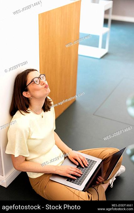 Bored businesswoman sitting with laptop on floor in office