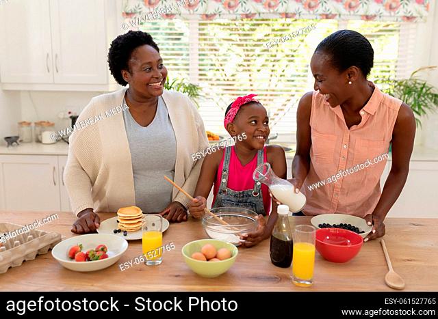 African american mother and grandmother teaching girl cooking in the kitchen