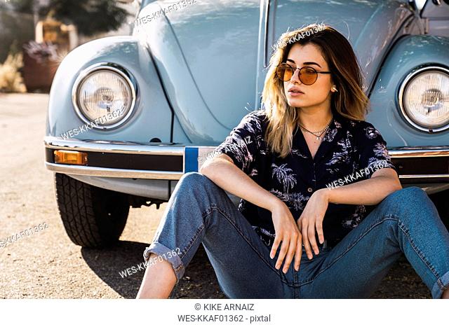 Young woman wearing sunglasses sitting outside at a vintage car