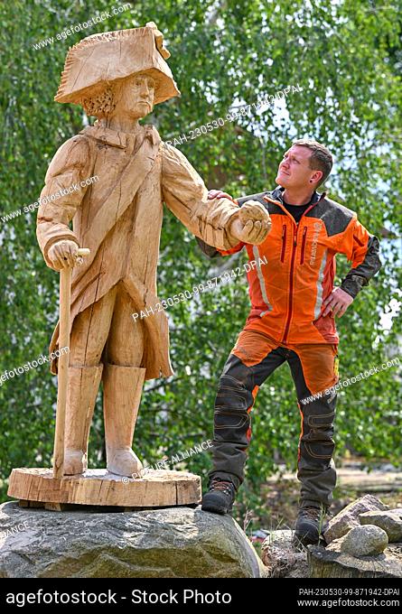 PRODUCTION - 23 May 2023, Brandenburg, Heinersdorf: Christian Mücke, chainsaw artist, stands next to the life-size wooden figure of Prussian King Frederick II...