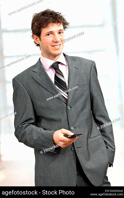 Young businessman standing with hand in pocket, using mobile phone, smiling