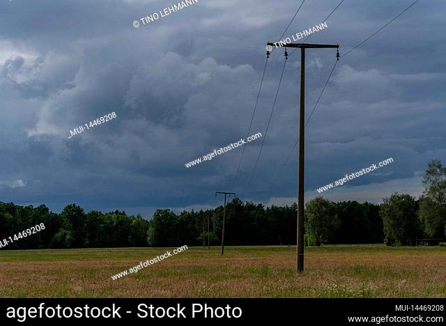 Large rain clouds over a large meadow near the town of Luckenwalde in Germany, electricity pylons stand on the meadow