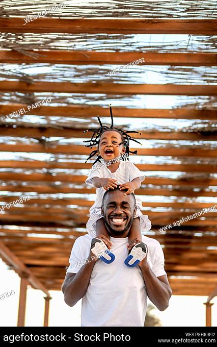 Cheerful man with eyes closed carrying daughter under roofing