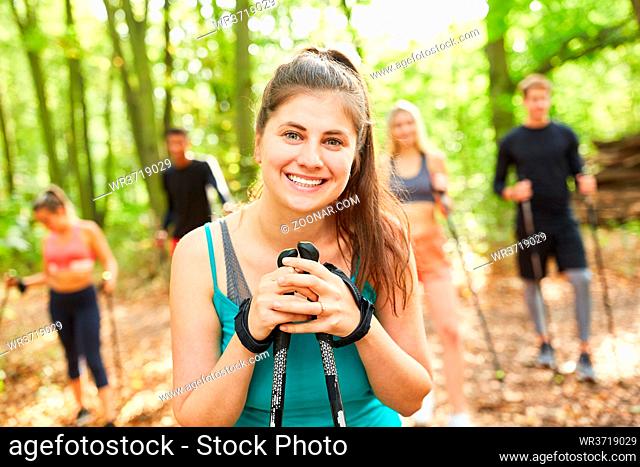Lächelnde junge Frau mit Freunden beim Nordic Walking in der Natur im Aktivurlaub