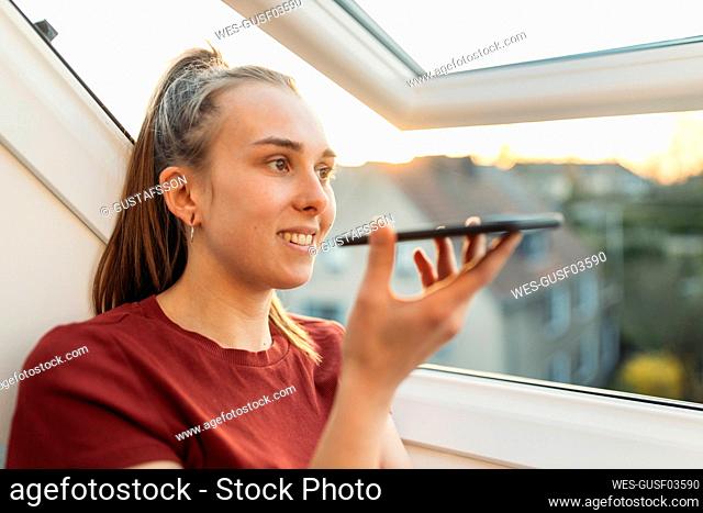 Young woman using smartphone at the window in backlight
