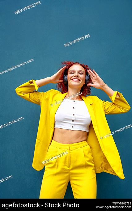 Young woman with red curly hair wearing headphones having fun listening music