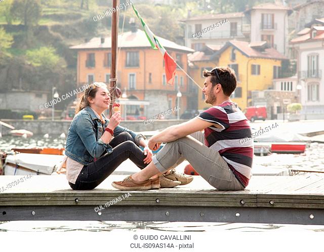 Couple sitting on pier eating ice cream cone at lake Mergozzo, Verbania, Piemonte, Italy
