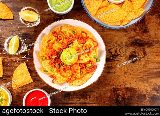 Nachos, tequila, and guacamole, shot from above on a dark rustic wooden background with a place for text