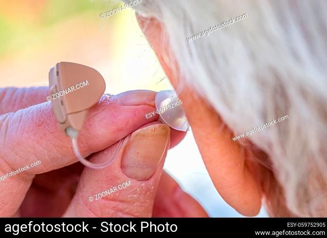 closeup senior woman inserting hearing aid in her ears