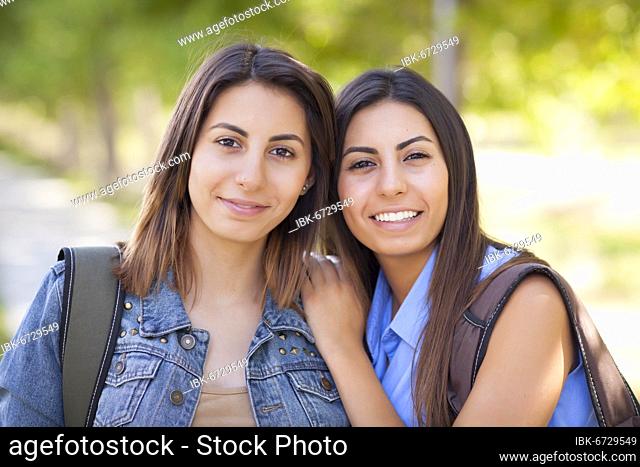 Young adult mixed-race twin sisters portrait wearing backpacks outside