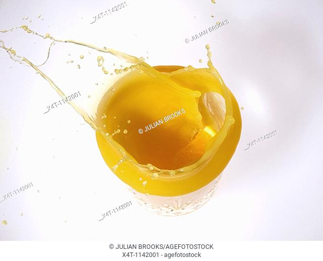 slice of orange splashing into a glass of orange juice from above