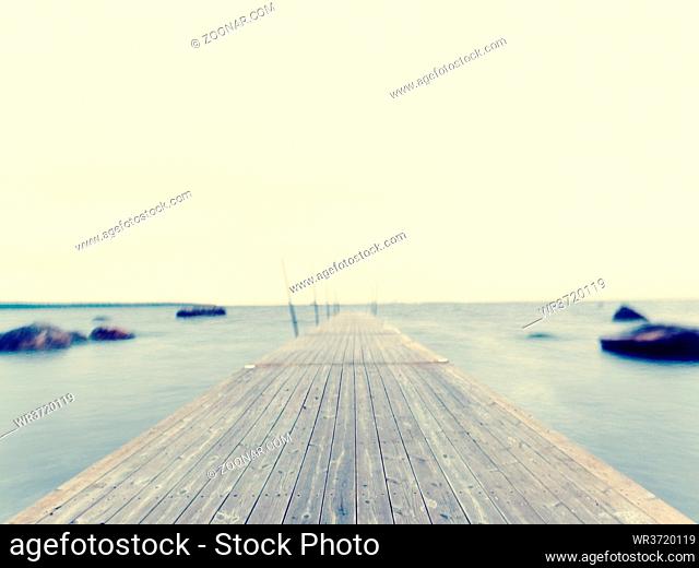 Empty wooden mole in water of blue lake. Old fishing wharf for hired boats and swimmers. Waves smooth by long exposure, cloudy sky