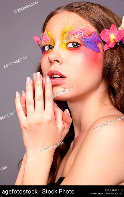 Portrait of teen girl with hand near face. Young female with unusual stylish make-up and false fashion feather eyelashes. Orchid flower in wavy hair