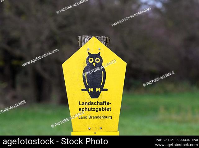 PRODUCTION - 21 November 2023, Brandenburg, Stahnsdorf: A sign next to a meadow and a forest shows a black eagle owl on a yellow background as a sign for a...