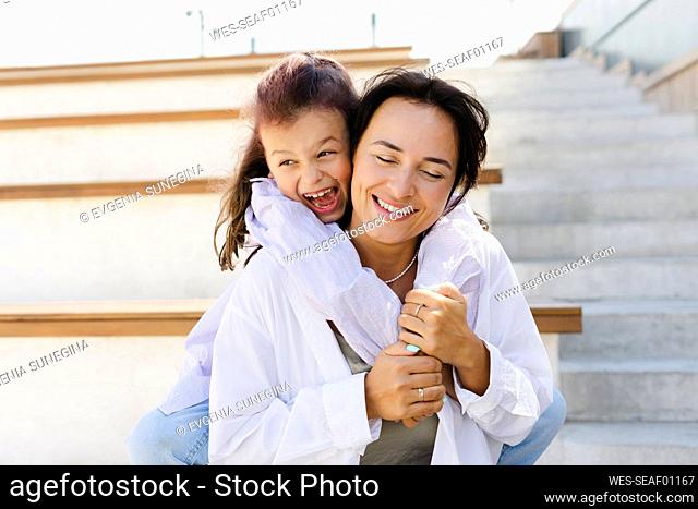 Cheerful daughter embracing mother with eyes closed