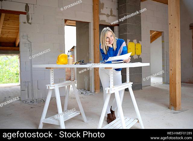 Female design professional with hand on chin looking away while leaning on table