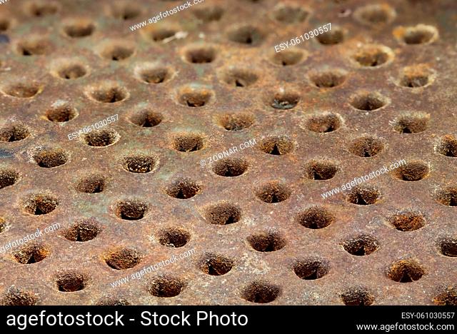 Rusty metal surface with round holes arranged in a row. Grunge background. Selective focus close-up image
