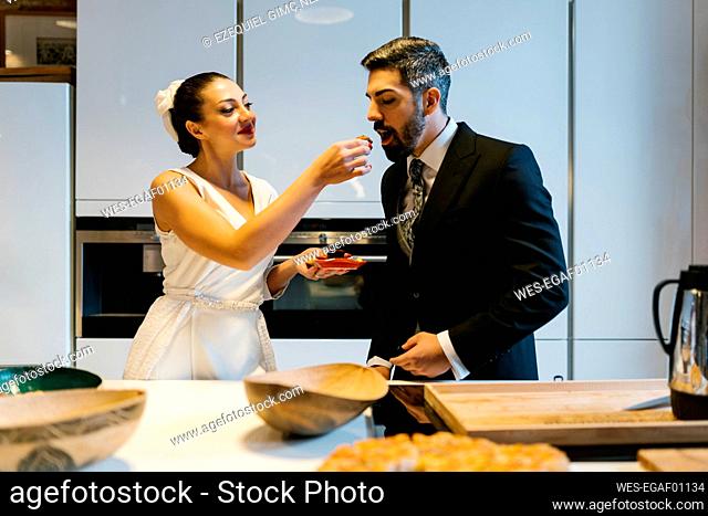 Young bride feeding groom in kitchen at home