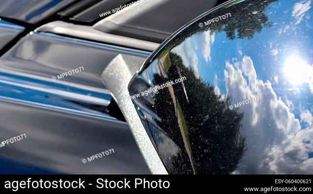 Reflections of a blue sky with clouds in the surface of a black sports car