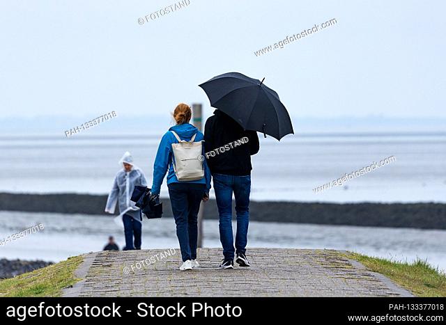 Harlesiel / Carolinensiel, Germany June 2020: Symbolic images - 2020 A woman and a man, with rain with umbrellas on the dike on the beach of Harlesiel