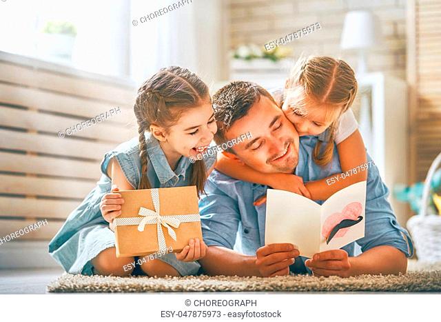 Happy father's day! Children daughters congratulating dad and giving him postcard and gift box. Daddy and girls smiling and hugging