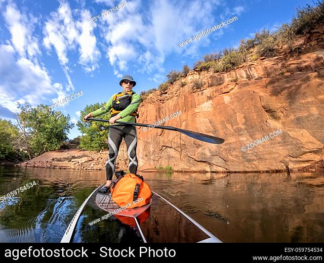senior man paddling a stand up paddleboard a mountain lake with sandstone cliffs - Horsetooth Reservoir , COlorado, in early fall scenery