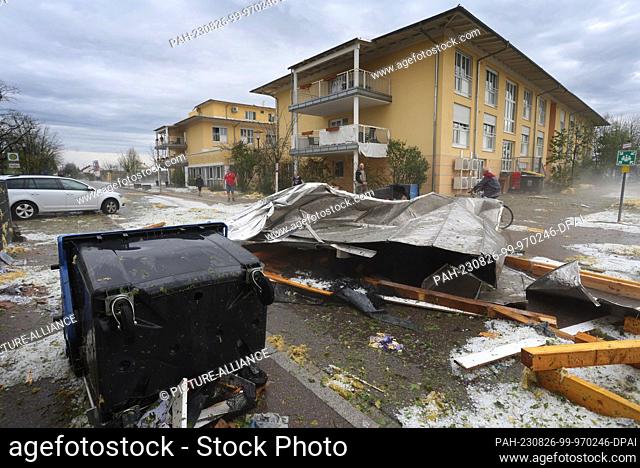 26 August 2023, Bavaria, Kissing: A roof of a senior citizen's home removed by the storm lies next to an overturned trash can in a parking lot Photo: Karl-Josef...