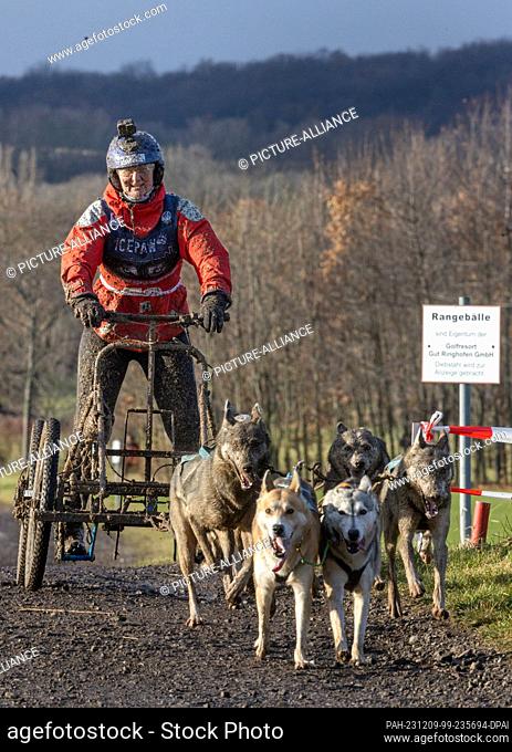 09 December 2023, Thuringia, Drei Gleichen: A mud-splattered musher crosses the finish line at the World Sleddog Association (WSA) Dryland Sled Dog World...