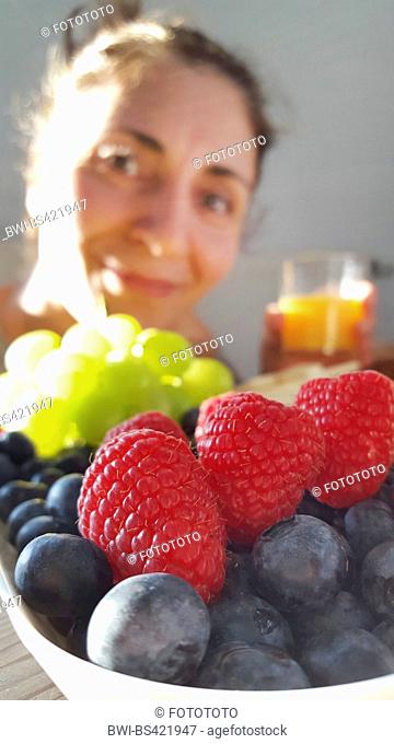 European red raspberry (Rubus idaeus), woman looking forward to a fruit bowl with raspberries, bluberries and grapes, dessert fruit, Germany