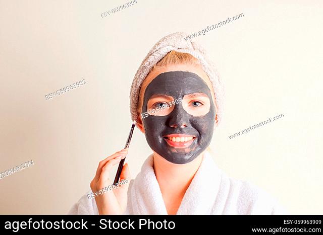 Smiling woman applying black charcoal mask on face at home