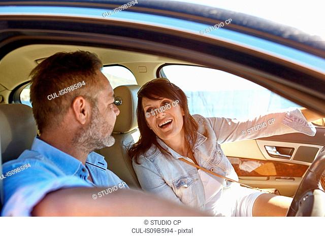 Couple in car, man driving, woman pointing ahead, laughing