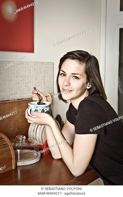 a smiling woman sitting in the kitchen while doing breakfast