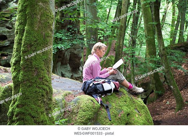 Germany, Rhineland-Palatinate, Eifel Region, South Eifel Nature Park, View of woman hiker sitting on bunter rock formations at beech tree forest