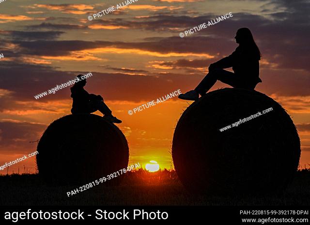 08 August 2022, Brandenburg, Jacobsdorf: Two friends are sitting on straw rolls in a field at sunset. Photo: Patrick Pleul/dpa